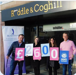 The Riddle & Coghill Interiors team outside the showroom holding up cards spelling out £2,600 and an MND Scotland sign