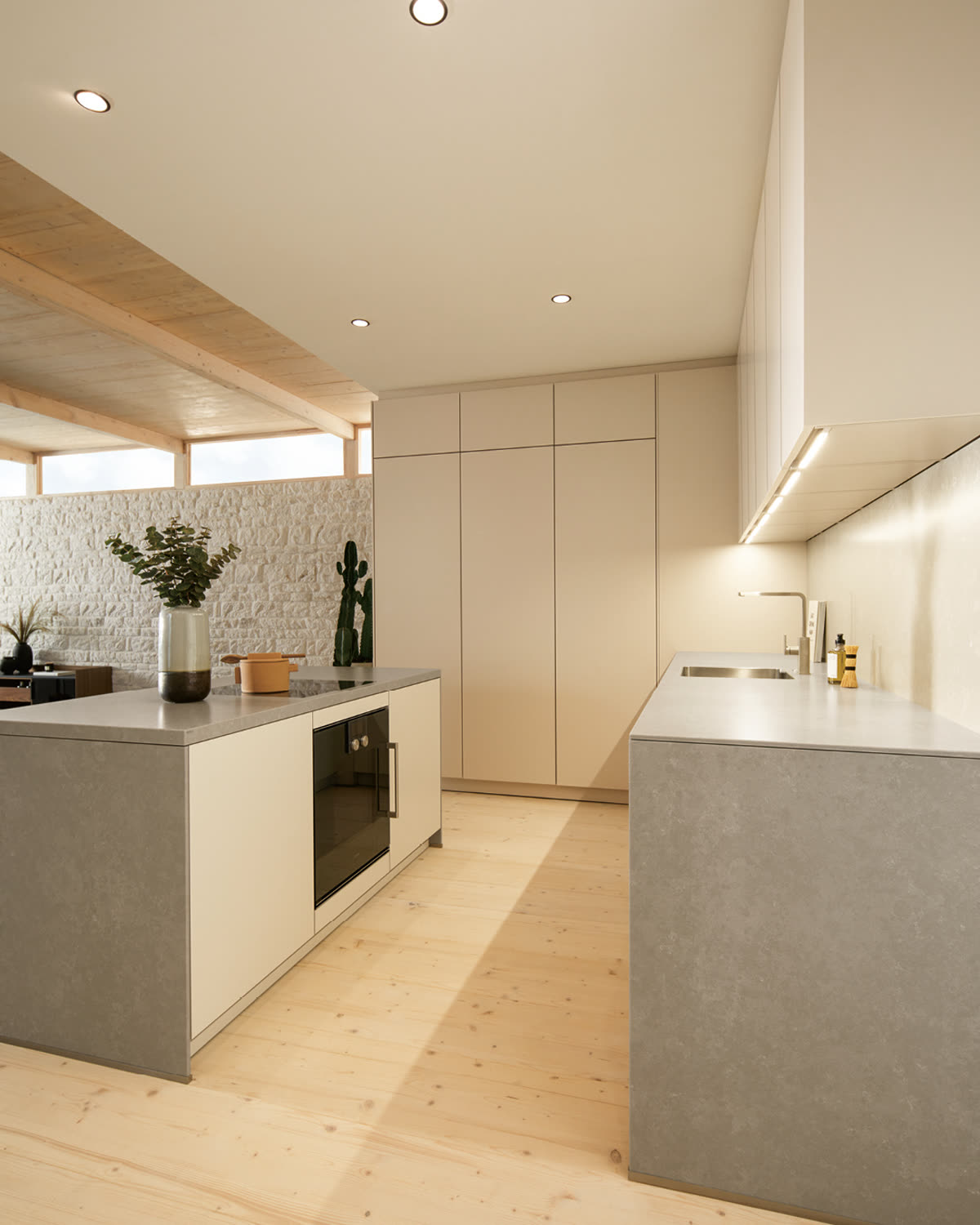 A pale kitchen island and worktop against an exposed stone wall, under a timber-beamed ceiling