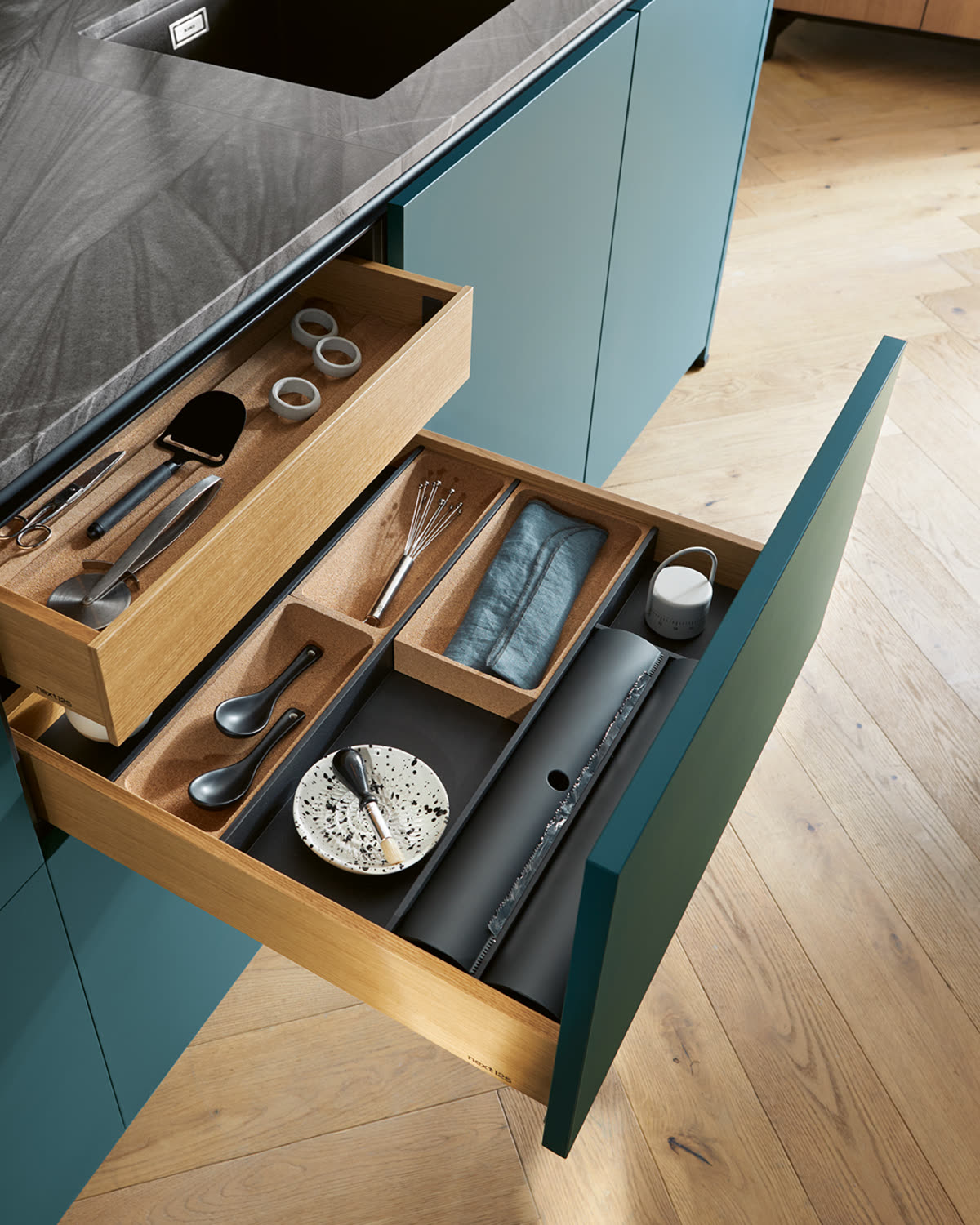 An open drawer with fitted oak cutlery and utensil dividers in a teal kitchen island
