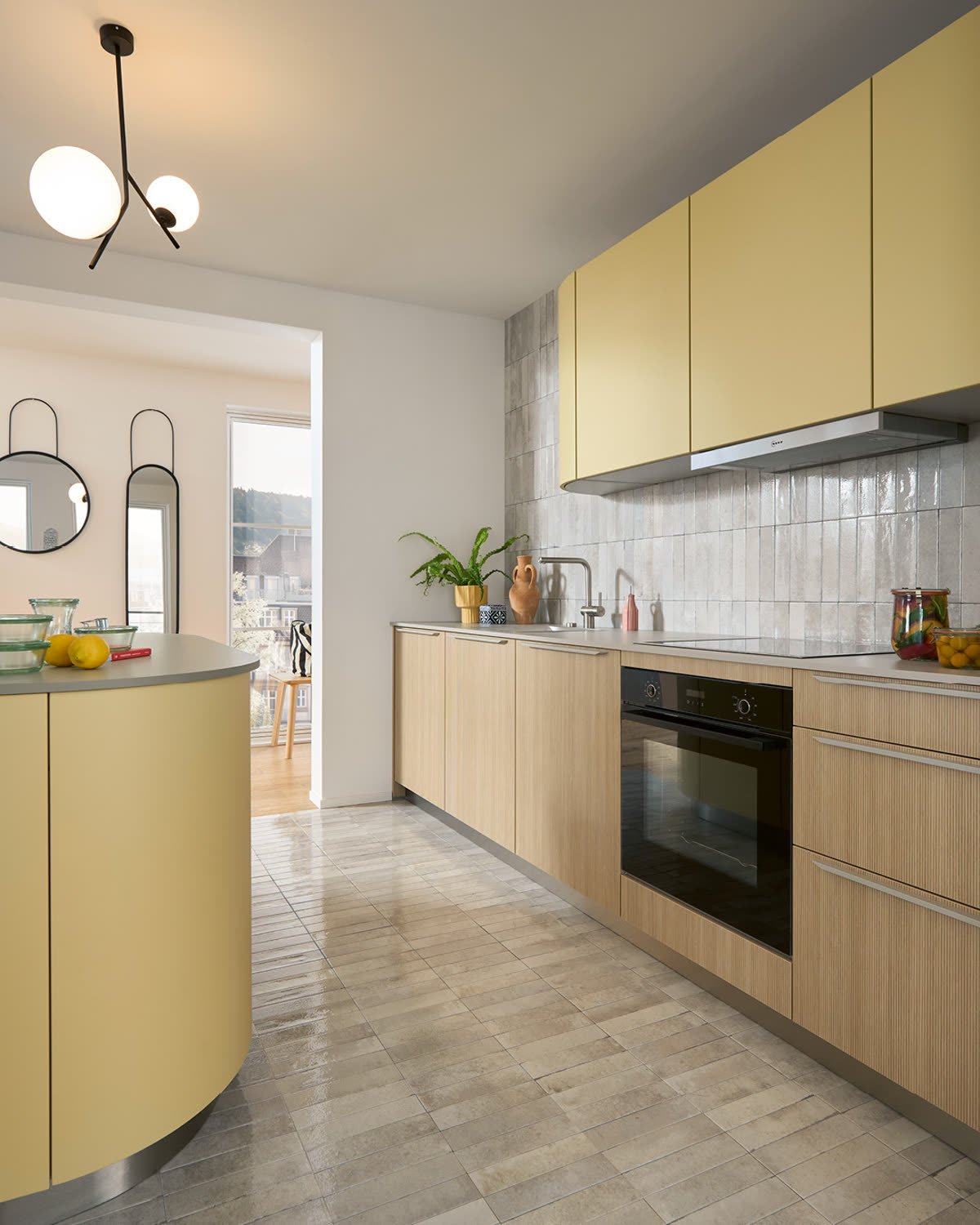 A pale yellow and oak galley kitchen with a curved island and pendant lighting